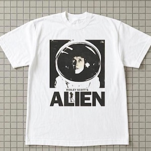 May include: White t-shirt featuring a black and white graphic from Ridley Scott's "Alien." The graphic shows a person in a space helmet with the film's title below. The shirt has short sleeves and a crew neck.
