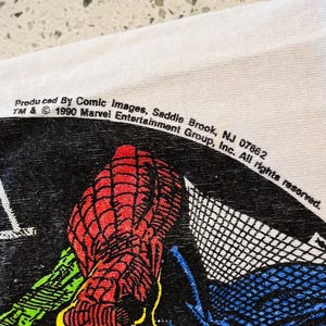May include: A white fabric surface featuring a black graphic print of a red-webbed character. The text reads: Produced By Comic Images, Saddle Brook, NJ 07662 TM & &copy; 1990 Marvel Entertainment Group, Inc. All rights reserved. The print includes green and blue.