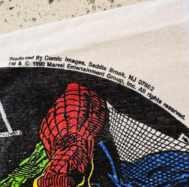 May include: A white fabric surface featuring a black graphic print of a red-webbed character. The text reads: Produced By Comic Images, Saddle Brook, NJ 07662 TM & &copy; 1990 Marvel Entertainment Group, Inc. All rights reserved. The print includes green and blue.