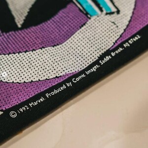 May include: A black fabric item featuring a purple and white graphic design with a halftone dot pattern. The text printed on the fabric reads: 1992 Marvel. Produced by Comic Images, Saddle Brook, NJ 07662. The material has a visible mesh texture.