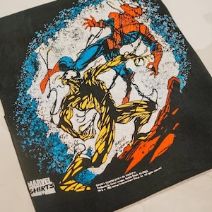 May include: A black t-shirt featuring a graphic print of Spider-Man in red and blue fighting a yellow and black creature. The design includes a blue speckled circular background, the Marvel Shirts logo, and copyright text dated 1992 at the bottom.