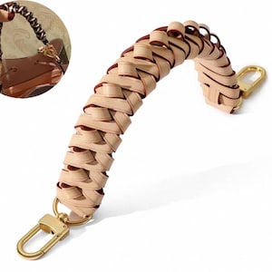 May include: A braided beige leather handbag strap with gold-colored hardware. The strap is curved and features a woven design. The hardware includes a clasp for easy attachment to a bag. The strap is shown against a white background.
