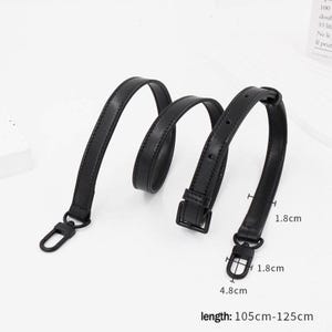 Puede incluir: Una correa de bolso de cuero negro con cierres metálicos y una hebilla. La correa mide aproximadamente 105-125 cm de largo y 1,8 cm de ancho. Los cierres miden 1,8 cm de ancho y 4,8 cm de largo.