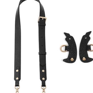 May include: Black leather handbag strap with gold-colored hardware, including a buckle, rivets, and clasps. The strap is shown with two matching black leather pieces with gold rings and rivets, designed for attaching to a bag.