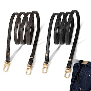 May include: Two leather purse straps, one in dark brown and the other in black, are displayed. Each strap is coiled and features gold-colored hardware, including clasps and rivets, for attachment to a bag.