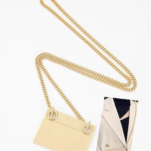 Peut inclure: Une pochette porte-cartes rectangulaire beige dotée de deux anneaux circulaires dorés fixés à une longue bandoulière en chaîne dorée. Le texte "Fit "ysl cardholder" pouch" est visible en haut. Un petit encart montre la pochette sur un blazer.