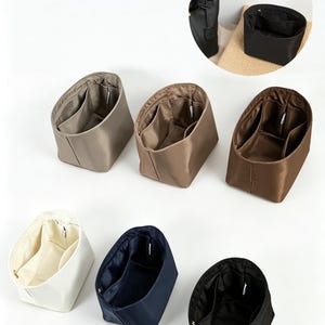 Op de afbeelding: Collectie handtassen organizers in verschillende kleuren, waaronder beige, bruin, marineblauw en zwart. Elke organizer heeft meerdere compartimenten en is ontworpen om in een handtas of tote bag te passen. De organizers zijn gemaakt van een gladde, duurzame stof.