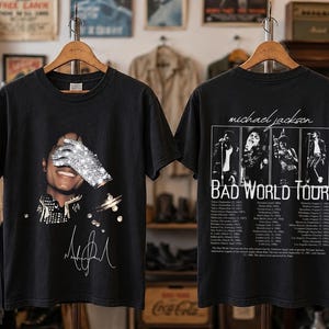 May include: A black short-sleeve t-shirt featuring a graphic of Michael Jackson with a sequined glove over his face on the front and a Bad World Tour graphic with tour dates and four black and white performance photos on the back.