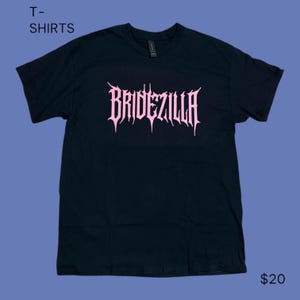 Puede incluir: Camiseta negra con la palabra "BRIDEZILLA" en rosa, con letras de estilo gótico en la parte delantera. La camiseta es de cuello redondo. Las palabras "T-SHIRTS" están en la esquina superior izquierda.