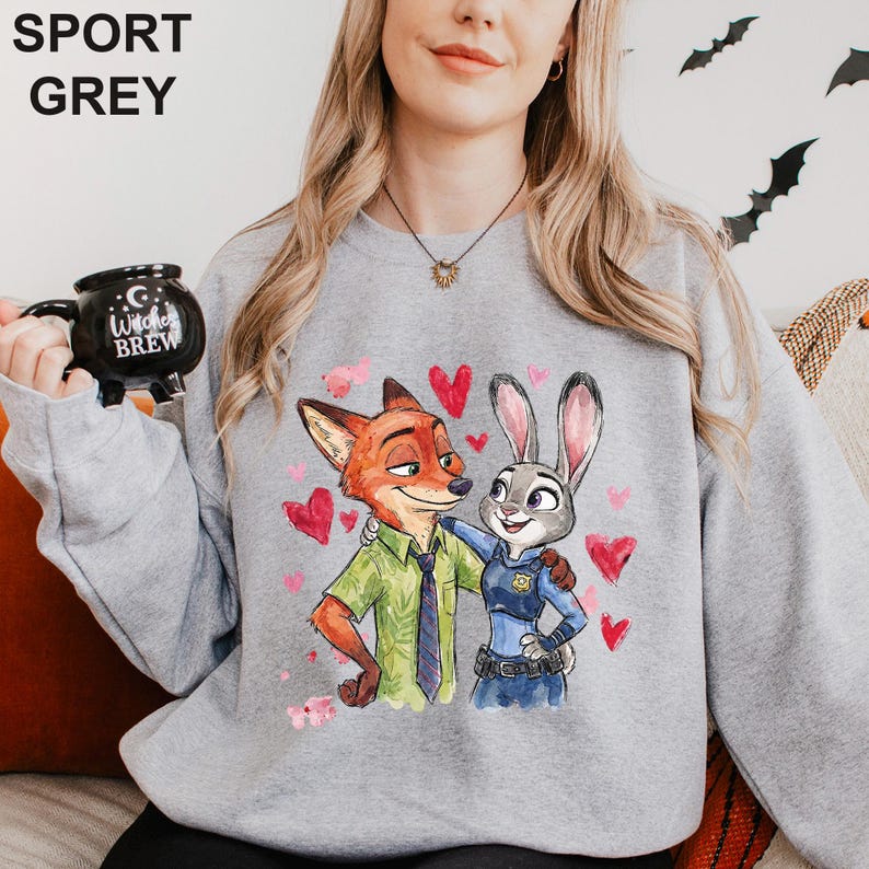 May include: Sport grey sweatshirt featuring a cartoon illustration of Nick Wilde and Judy Hopps from Zootopia, surrounded by red hearts. The sweatshirt has the text "SPORT GREY" at the top. A black mug with the text "Witches Brew" is held in the image.