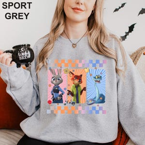 May include: Sport grey sweatshirt with cartoon characters Judy Hopps, Nick Wilde, and a snake. The design includes a colourful checkered pattern and stars. The sweatshirt is a light grey colour.