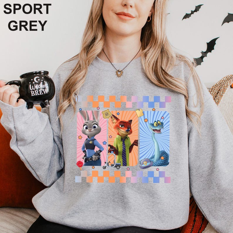 May include: Sport grey sweatshirt with cartoon characters Judy Hopps, Nick Wilde, and a snake. The design includes a colourful checkered pattern and stars. The sweatshirt is a light grey colour.