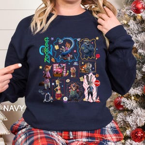 May include: Navy blue sweatshirt featuring a colorful collage of characters from the animated movie "Zootopia." The design includes various characters in square and rectangular frames, with the word "Zootopia" in green. The word "NAVY" is printed on the bottom left.