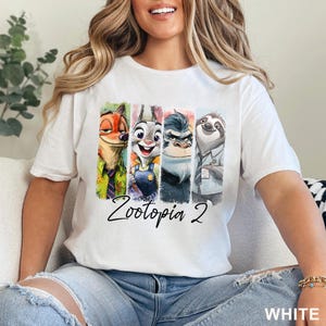 May include: White t-shirt with a vibrant graphic of Zootopia characters: a fox, rabbit, gorilla, and sloth. The text "Zootopia 2" is written below the characters. The word "WHITE" is printed in the bottom right corner of the t-shirt.