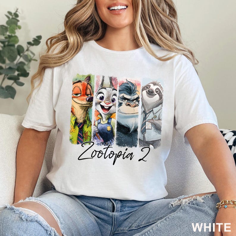 May include: White t-shirt with a vibrant graphic of Zootopia characters: a fox, rabbit, gorilla, and sloth. The text "Zootopia 2" is written below the characters. The word "WHITE" is printed in the bottom right corner of the t-shirt.