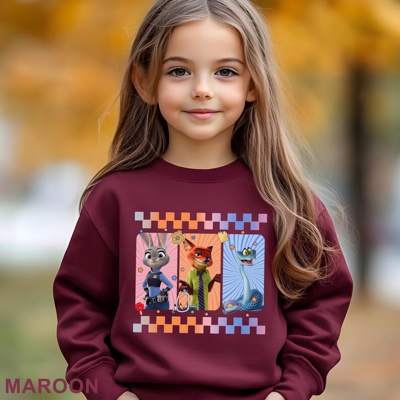 May include: A maroon sweatshirt with a design featuring three Zootopia cartoon characters: Judy Hopps, Nick Wilde, and a snake. The design is framed with a checkered pattern. The word "MAROON" is printed at the bottom.