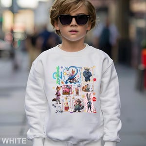May include: White sweatshirt featuring a colorful graphic of characters from the animated film "Zootopia." The design includes images of a fox, a bunny, and other animals. The word "Zootopia" is written in green. The word "WHITE" is printed at the bottom.