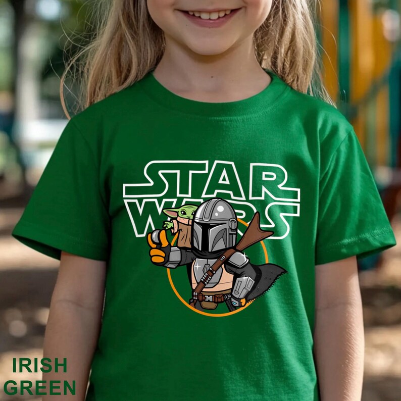 May include: Irish green t-shirt featuring a Star Wars graphic. The design includes the text "STAR WARS" in white, along with an illustration of The Mandalorian and Grogu. The shirt is a solid green color.
