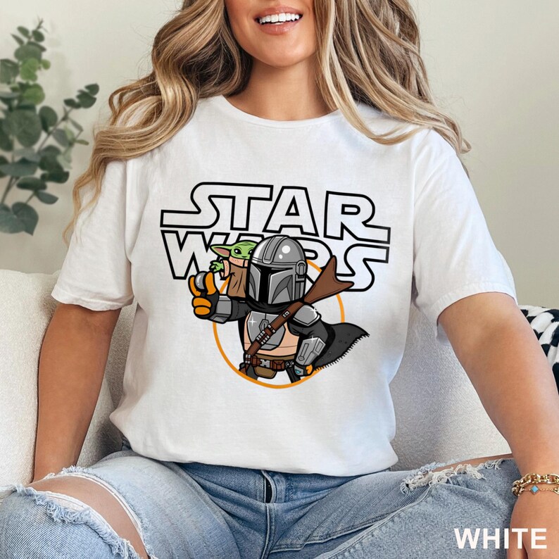 May include: White t-shirt featuring a cartoon illustration of The Mandalorian and Grogu from Star Wars. The design includes the Star Wars logo in black and white, with the word "WHITE" printed at the bottom.