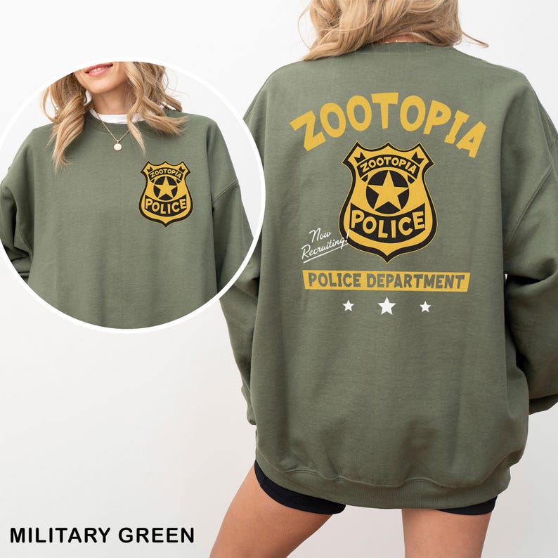 May include: Military green sweatshirt featuring a Zootopia Police Department badge on the front and back. The back design includes the word "Zootopia" in yellow, a police badge, and the text "Police Department".