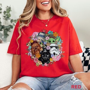 May include: Red t-shirt featuring a floral arrangement with Star Wars characters including Chewbacca, Darth Vader, a Stormtrooper, R2-D2, and Grogu. The word "RED" is printed at the bottom right.