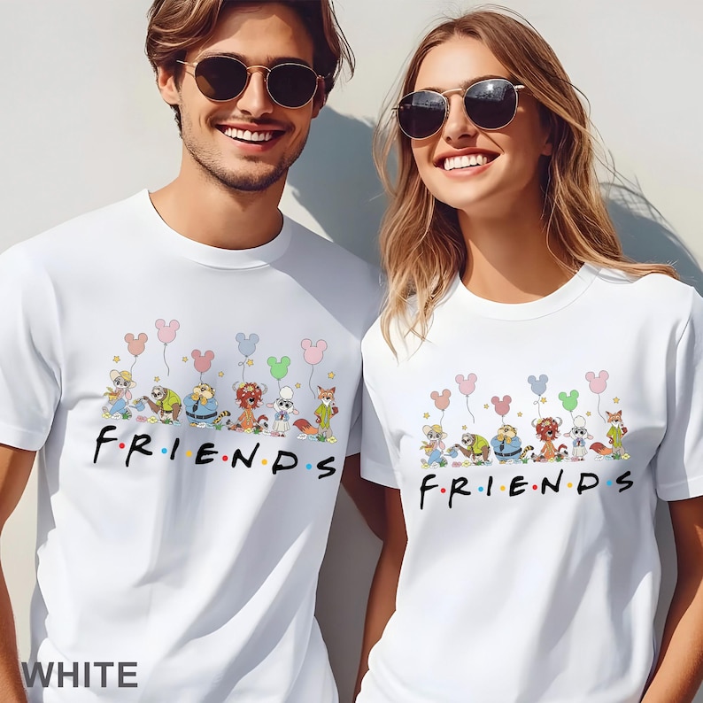 May include: White t-shirts with a cartoon design of animal characters holding balloons and the word "FRIENDS". The shirts are worn by two people. The design is in a playful font.