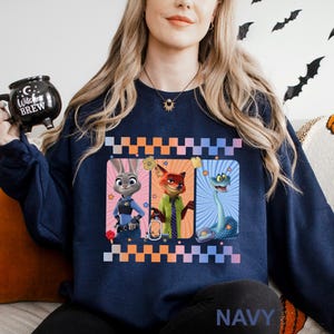 May include: Navy blue sweatshirt with a vibrant graphic of three cartoon characters. The design showcases a bunny, a fox, and a snake, each within a framed panel. The word "NAVY" is printed at the bottom of the sweatshirt.