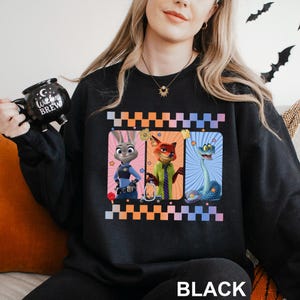 May include: Black sweatshirt with a design featuring three cartoon characters in rectangular frames with a chequered border. The characters include a rabbit, a fox, and a snake. The word "BLACK" is printed at the bottom.