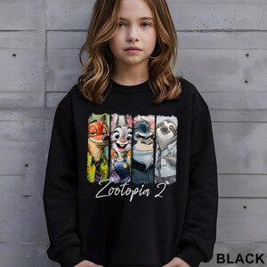 Op de afbeelding: Zwarte sweatshirt met een kleurrijke afbeelding van personages uit "Zootopia 2", waaronder Nick Wilde, Judy Hopps, Chief Bogo en Flash. De woorden "Zootopia 2" staan in witte letters onder de personages. Het woord "BLACK" staat rechtsonder.