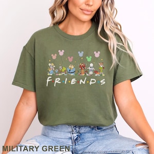 May include: Military green t-shirt with a cartoon design of animal characters holding Mickey Mouse-shaped balloons. The word "FRIENDS" is printed in a colourful font across the front.