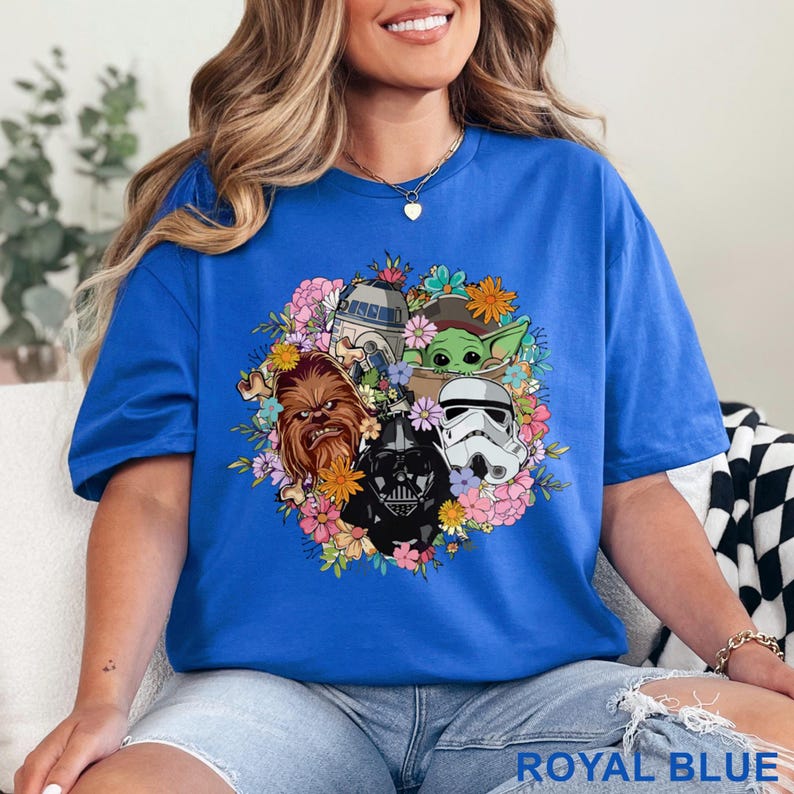 May include: Royal blue t-shirt featuring a floral arrangement with Star Wars characters including Darth Vader, Chewbacca, and a Stormtrooper. The shirt also features R2-D2 and Grogu. The text "ROYAL BLUE" is at the bottom.