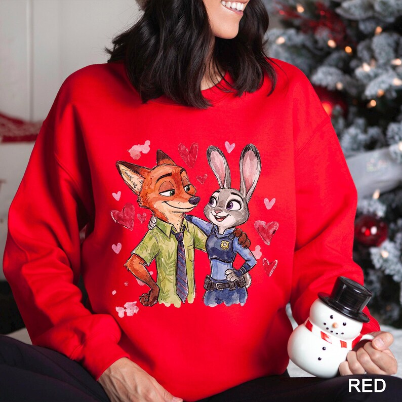 May include: A red sweatshirt featuring a cartoon illustration of a fox and a rabbit embracing, surrounded by heart shapes. The fox is wearing a green shirt and tie, while the rabbit is in a police uniform. The word "RED" is printed in white at the bottom.