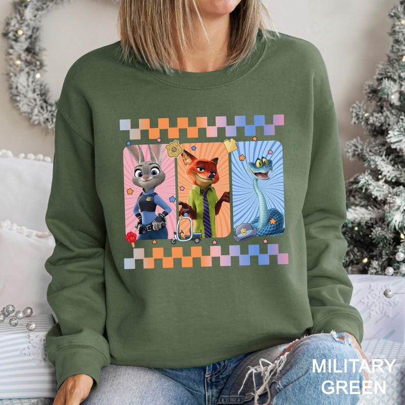 May include: Military green sweatshirt with three cartoon characters in rectangular frames and a checkered border. The characters are a rabbit in a police uniform, a fox in a suit, and a snake. The sweatshirt has the words "MILITARY GREEN" printed on it.