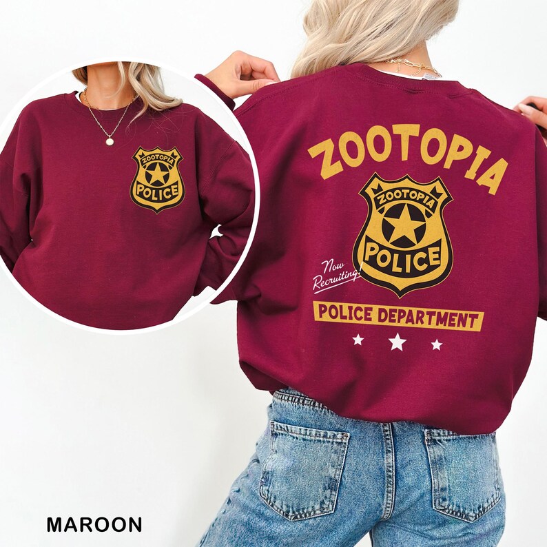 May include: Maroon sweatshirt featuring a Zootopia Police Department badge on the front and back. The back of the sweatshirt has the words "ZOOTOPIA" and "POLICE DEPARTMENT" in gold lettering. The sweatshirt is made of a soft material.