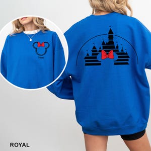 Pu&ograve; includere: Felpa blu reale con un contorno nero di Minnie Mouse e un fiocco rosso sul davanti. Il retro mostra un disegno di castello nero con un fiocco rosso. La parola "Name" &egrave; sotto il contorno di Minnie Mouse.