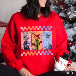 May include: A red sweatshirt with a design featuring three cartoon characters in rectangular frames. The characters are a rabbit in a police uniform, a fox in a green shirt, and a blue snake. The top of the sweatshirt has a checkered pattern.