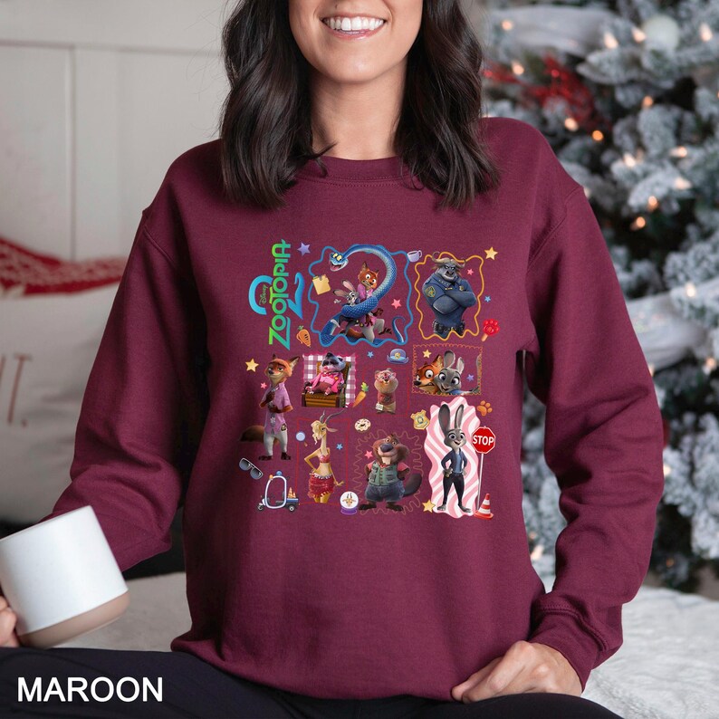 May include: Maroon sweatshirt featuring a colorful graphic of characters from the animated film "Zootopia." The design includes the film's title and various animal characters in a grid-like arrangement. The sweatshirt is a solid maroon color.
