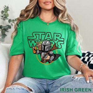 May include: Irish green t-shirt featuring a Star Wars graphic. The design includes the Star Wars logo, The Mandalorian, and Grogu. The Mandalorian is holding a weapon and Grogu is in a carrier. The text "IRISH GREEN" is at the bottom.