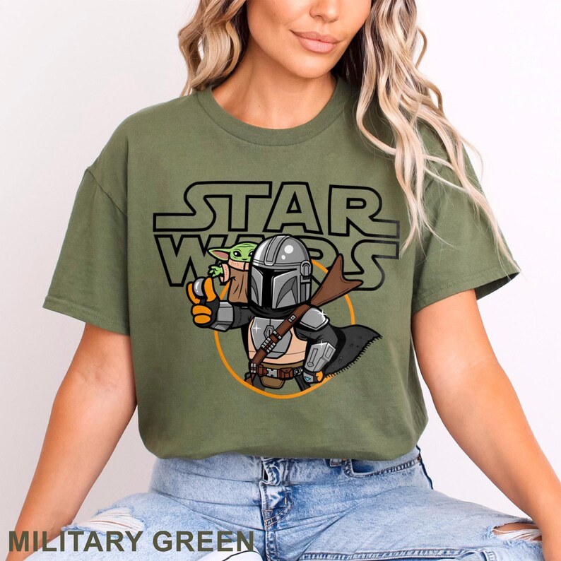 May include: Military green t-shirt featuring a cartoon illustration of The Mandalorian and Grogu from Star Wars. The design includes the Star Wars logo in black. The shirt is a comfortable, casual style.