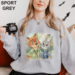 Puede incluir: Sudadera gris deportiva con un gr&aacute;fico colorido de un zorro y un conejo. El zorro lleva una camisa verde y el conejo un uniforme de polic&iacute;a azul. La sudadera tiene las palabras "SPORT GREY" impresas en la parte superior.