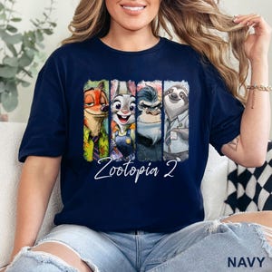 May include: Navy blue t-shirt with a vibrant graphic of Zootopia characters: a fox, rabbit, gorilla, and sloth. The text "Zootopia 2" is in white script. The word "NAVY" is printed at the bottom. A fun, colourful design.