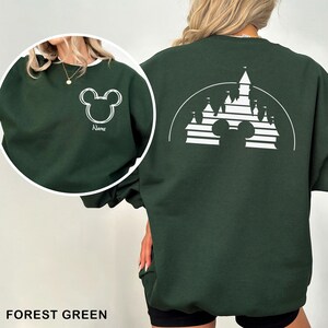 Pu&ograve; includere: Felpa verde foresta con un contorno bianco di Mickey Mouse sul davanti e un disegno di castello sul retro. Il design anteriore include la parola "Name" sotto il contorno di Mickey Mouse. La felpa &egrave; di colore unito con scollo tondo.