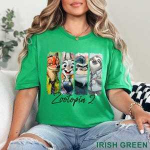May include: A green crew neck t-shirt with a graphic of Zootopia characters, including Nick Wilde, Judy Hopps, Chief Bogo, and Flash. The text "Zootopia 2" is written in a black script font. The shirt is a vibrant Irish green.