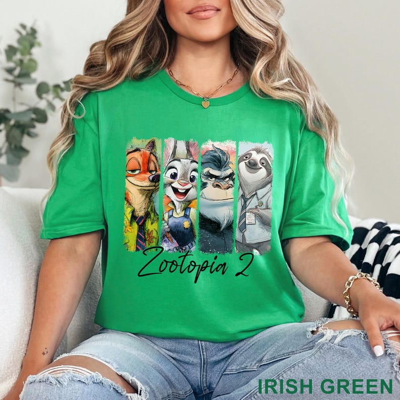 May include: A green crew neck t-shirt with a graphic of Zootopia characters, including Nick Wilde, Judy Hopps, Chief Bogo, and Flash. The text "Zootopia 2" is written in a black script font. The shirt is a vibrant Irish green.
