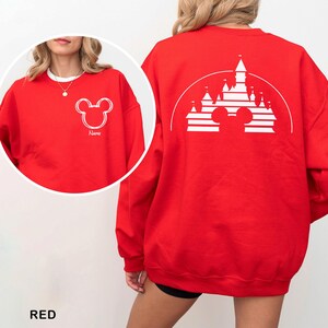 Pu&ograve; includere: Felpa rossa con un contorno bianco di Mickey Mouse sul davanti e la parola "Name" sotto. Il retro mostra un disegno di castello bianco con una silhouette di Mickey Mouse. La parola "RED" &egrave; nella parte inferiore dell'immagine.