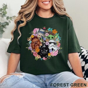 May include: Forest green t-shirt featuring a floral arrangement with Star Wars characters including Darth Vader, Chewbacca, R2-D2, a Stormtrooper, and Grogu. The text "FOREST GREEN" is printed at the bottom of the shirt.