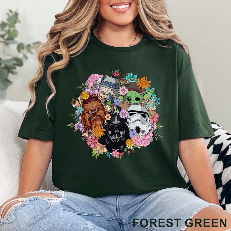 May include: Forest green t-shirt featuring a floral arrangement with Star Wars characters including Darth Vader, Chewbacca, R2-D2, a Stormtrooper, and Grogu. The text "FOREST GREEN" is printed at the bottom of the shirt.