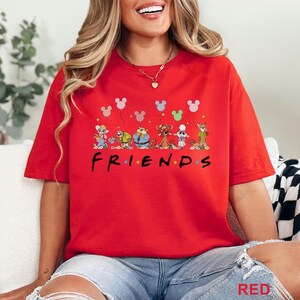 May include: A red t-shirt with the word "FRIENDS" in black, and cartoon characters with Mickey Mouse balloon graphics. The shirt is a bright red colour.