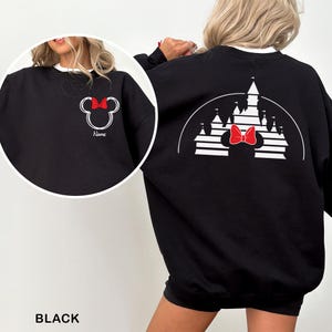 Pu&ograve; includere: Felpa nera con un design di Minnie Mouse, con un fiocco rosso e una silhouette di castello sul retro. La parte anteriore presenta una testa di Minnie Mouse con un fiocco rosso e la parola "Name". La felpa ha un colletto bianco.