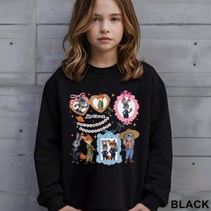 Op de afbeelding: Zwarte sweatshirt met illustraties van Zootopia-personages in hartvormige en ovale frames. Het woord "ZOOTOPIA" is in het wit gedrukt. De sweatshirt heeft een ronde hals en lange mouwen. Het woord "BLACK" staat rechtsonder.